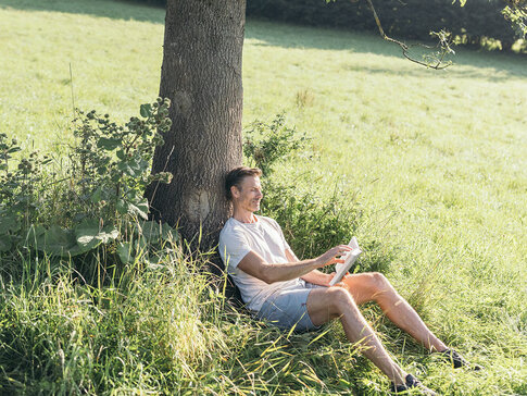 Der Mann sitzt angelehnt an einem Baum mit einem Buch